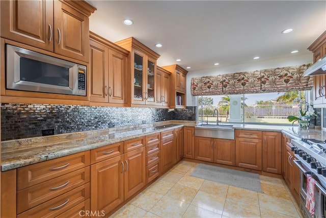 kitchen with appliances with stainless steel finishes, brown cabinetry, glass insert cabinets, and a sink