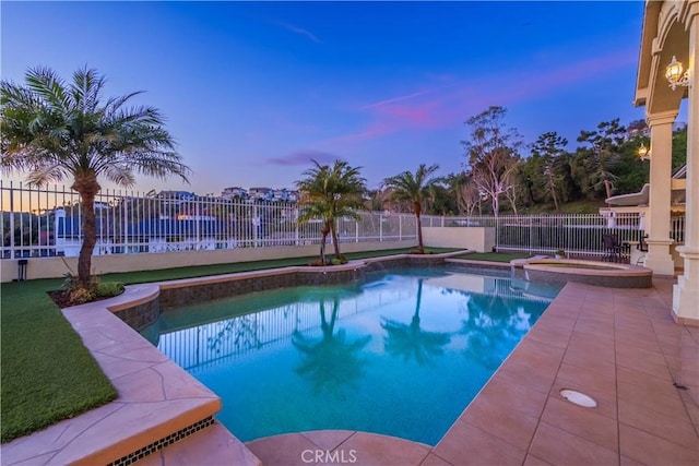 pool at dusk with an in ground hot tub, fence, and a fenced in pool