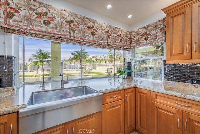 kitchen with plenty of natural light, light stone counters, brown cabinets, and a sink