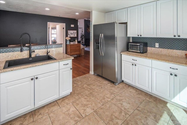 kitchen with white cabinets, tasteful backsplash, stainless steel refrigerator with ice dispenser, and a sink