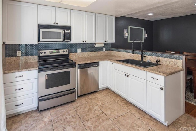 kitchen featuring light stone counters, stainless steel appliances, a sink, white cabinets, and tasteful backsplash