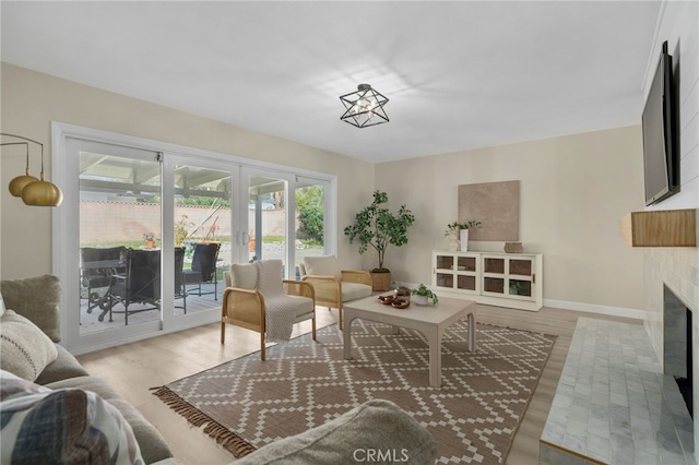 living area featuring a fireplace with flush hearth, baseboards, and wood finished floors