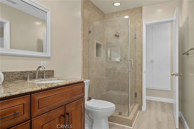 bathroom with a stall shower, baseboards, toilet, wood finished floors, and vanity