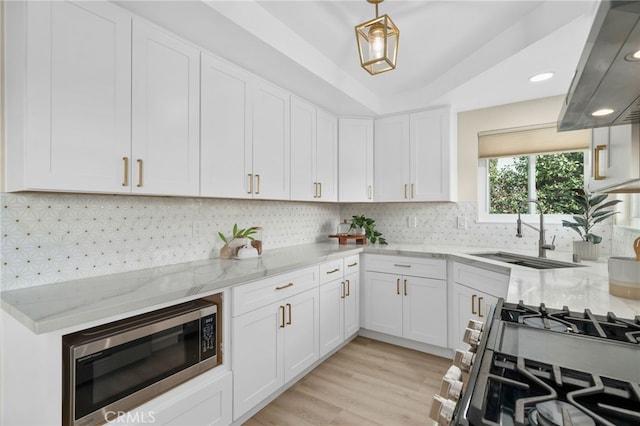 kitchen with stainless steel appliances, backsplash, white cabinets, a sink, and light stone countertops