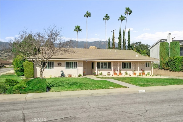 single story home featuring a mountain view, a front lawn, and stucco siding