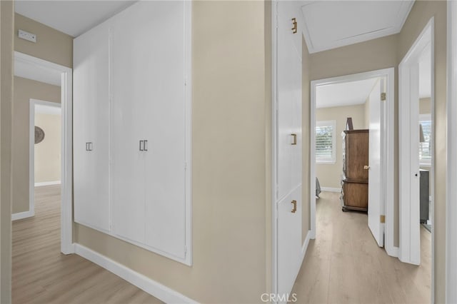 hallway featuring attic access, baseboards, and light wood finished floors