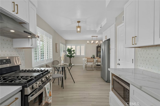 kitchen with tasteful backsplash, white cabinets, appliances with stainless steel finishes, light wood-type flooring, and under cabinet range hood