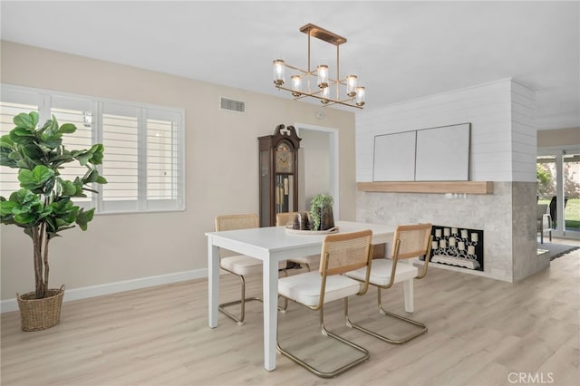 dining area with visible vents, light wood-style flooring, an inviting chandelier, a large fireplace, and baseboards