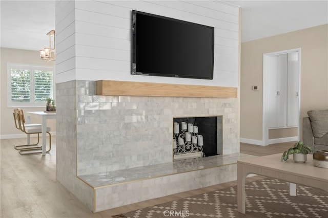 living area featuring a fireplace with raised hearth, a notable chandelier, wood finished floors, and baseboards