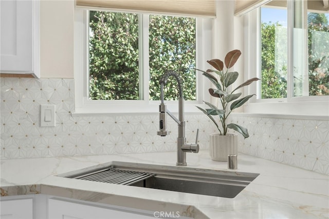 room details with tasteful backsplash, light stone counters, a sink, and white cabinets