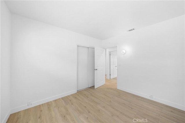 spare room featuring light wood-type flooring, visible vents, and baseboards