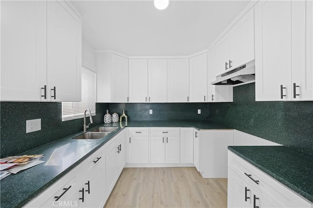 kitchen featuring dark countertops, under cabinet range hood, white cabinets, and a sink