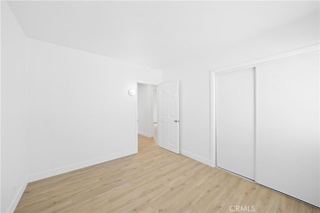 unfurnished bedroom with light wood-type flooring, a closet, and baseboards