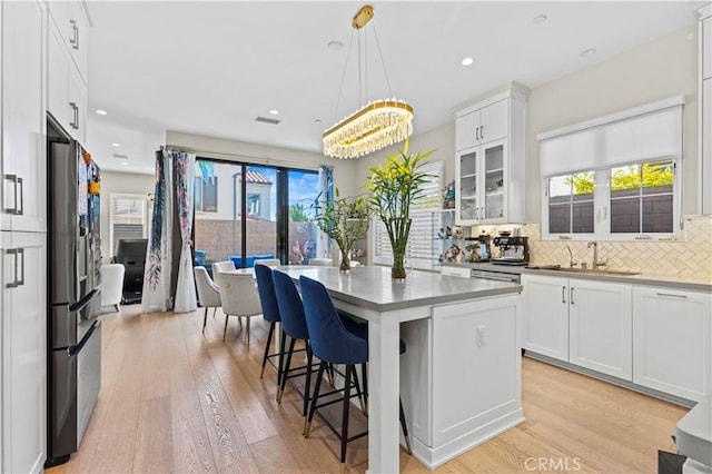 kitchen with a kitchen island, white cabinetry, a sink, and decorative light fixtures