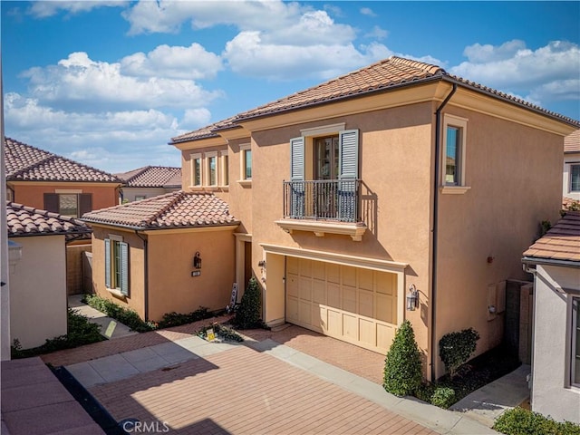 mediterranean / spanish home with a garage, a balcony, a tiled roof, decorative driveway, and stucco siding