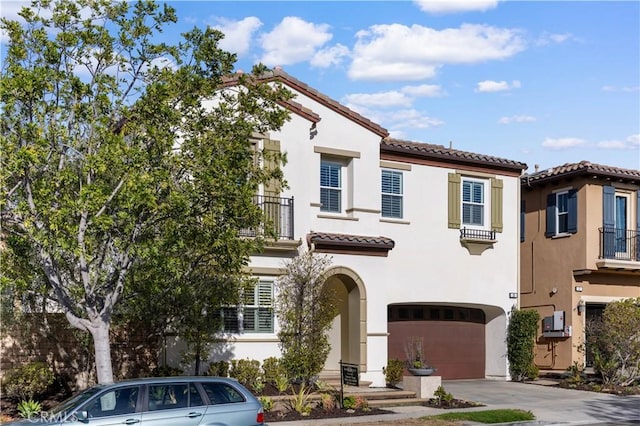 mediterranean / spanish-style house featuring an attached garage, a balcony, a tiled roof, concrete driveway, and stucco siding