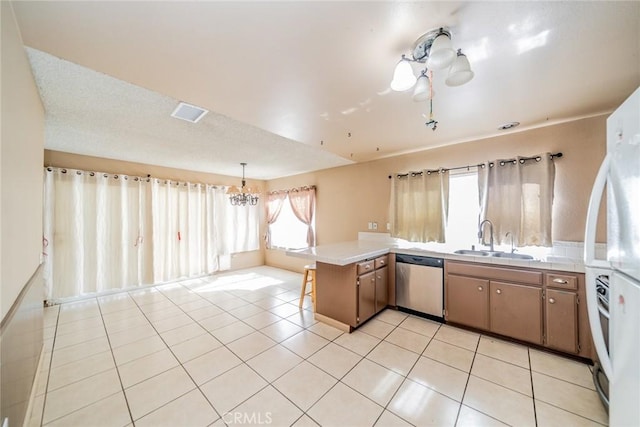 kitchen featuring stainless steel dishwasher, freestanding refrigerator, light tile patterned flooring, a sink, and a peninsula