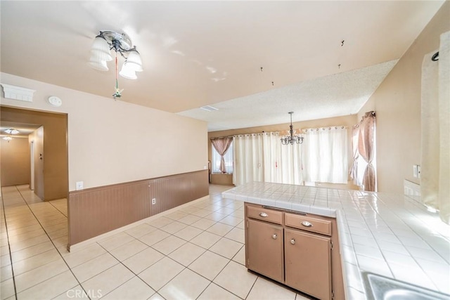 kitchen featuring tile countertops, light tile patterned floors, a peninsula, and wainscoting