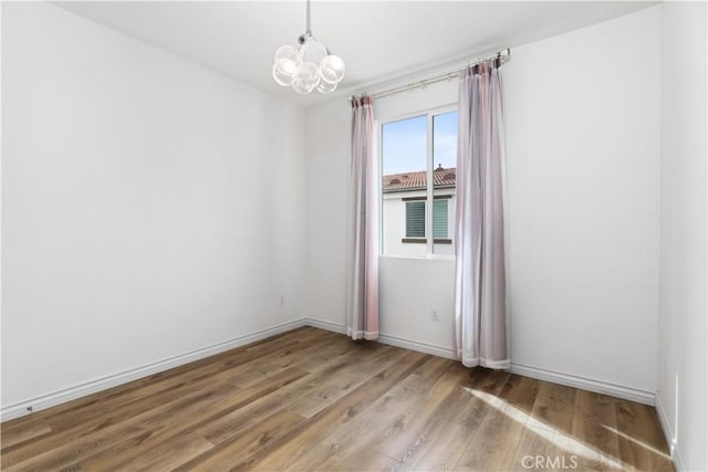 unfurnished room featuring a notable chandelier, light wood-style flooring, and baseboards