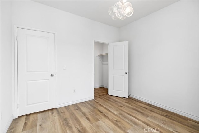 unfurnished bedroom featuring a chandelier, a closet, baseboards, and light wood finished floors