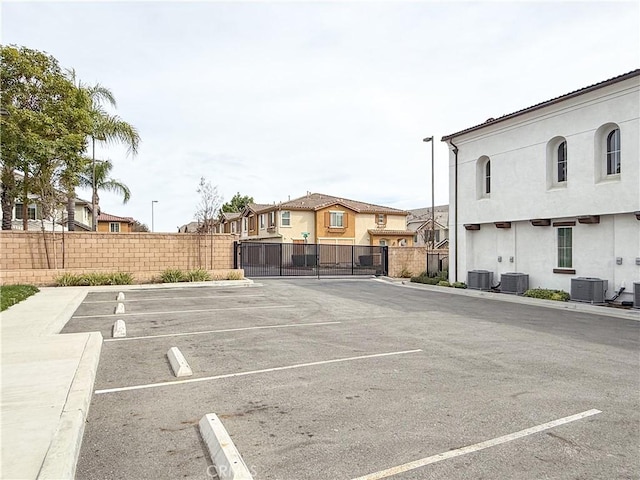 uncovered parking lot featuring a residential view, a gate, and fence