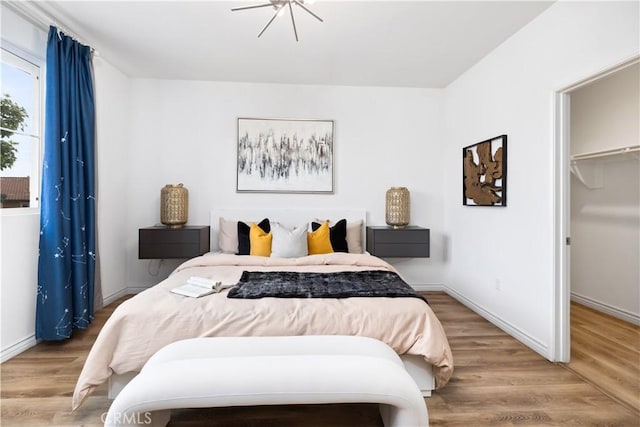 bedroom with a closet, baseboards, a walk in closet, and wood finished floors