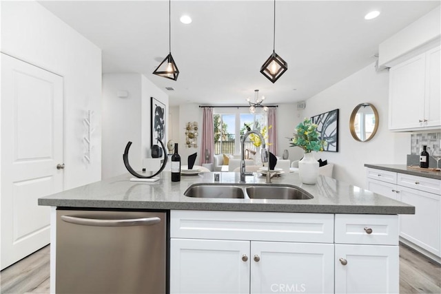 kitchen featuring white cabinets, decorative backsplash, open floor plan, stainless steel dishwasher, and a sink