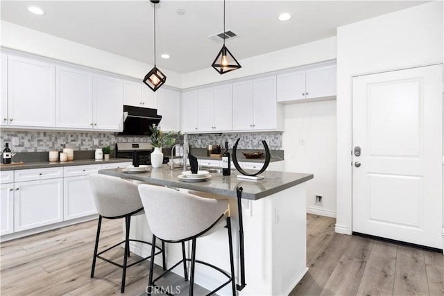 kitchen with tasteful backsplash, dark countertops, white cabinets, and visible vents