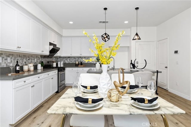 kitchen with under cabinet range hood, visible vents, white cabinets, tasteful backsplash, and gas range