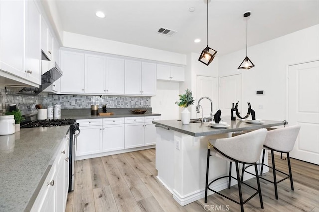 kitchen featuring gas stove, visible vents, decorative backsplash, and white cabinetry