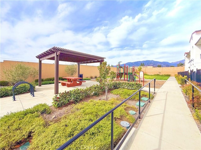 surrounding community featuring playground community, fence, a mountain view, and a pergola