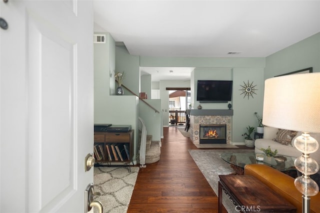 living area with a tile fireplace, visible vents, stairway, and wood finished floors