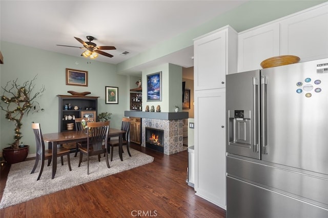 dining space with dark wood-style floors, visible vents, ceiling fan, and a lit fireplace