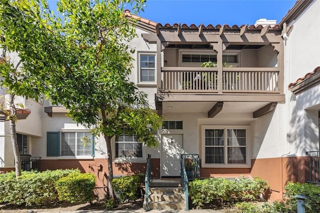 view of front of home featuring a tile roof, a balcony, and stucco siding