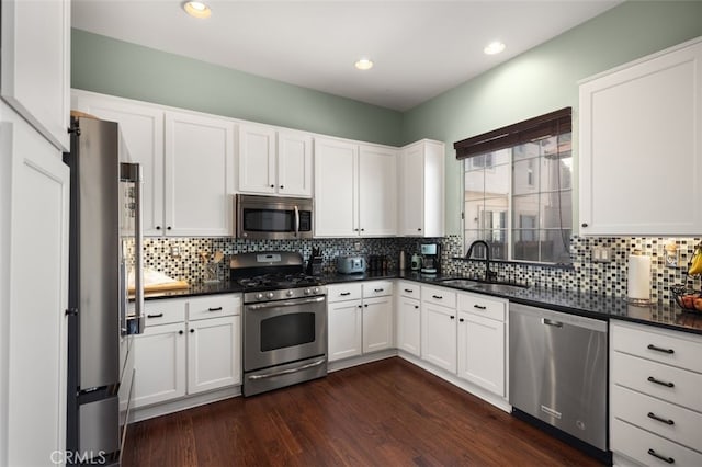 kitchen with stainless steel appliances, dark countertops, dark wood-type flooring, white cabinetry, and a sink