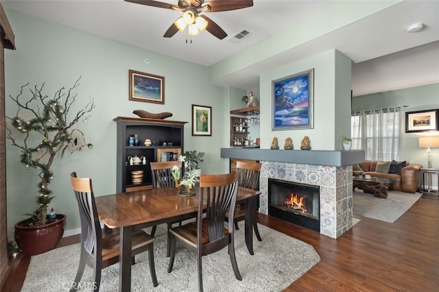 dining room with ceiling fan, visible vents, a fireplace, and wood finished floors