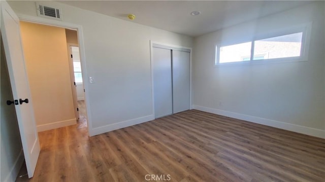 unfurnished bedroom featuring a closet, visible vents, baseboards, and wood finished floors