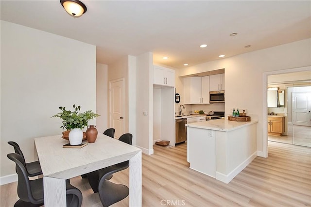 kitchen featuring stainless steel appliances, a peninsula, a sink, white cabinetry, and light wood finished floors