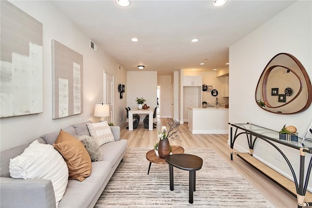 living area with baseboards, light wood-type flooring, visible vents, and recessed lighting