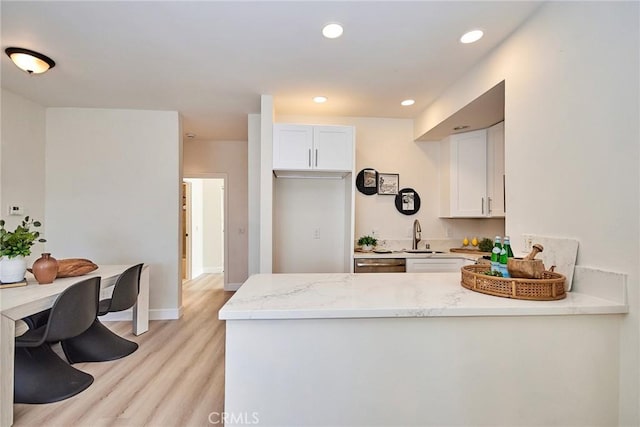 kitchen featuring light wood-type flooring, white cabinetry, dishwasher, and a peninsula