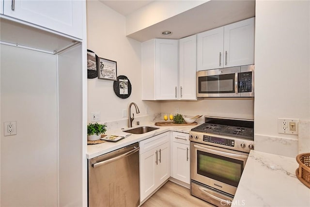 kitchen with stainless steel appliances, light stone counters, a sink, and white cabinetry