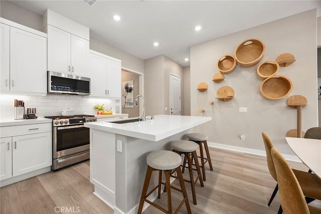 kitchen with light countertops, appliances with stainless steel finishes, a center island with sink, and white cabinets