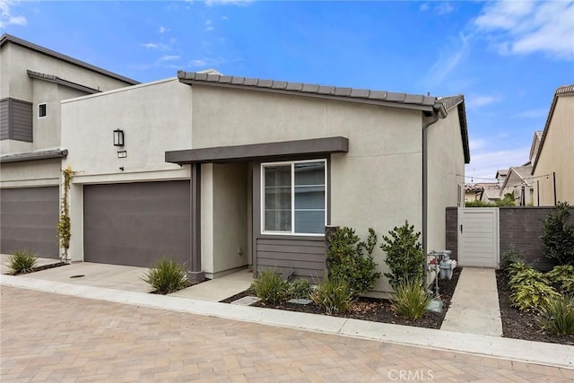 view of front of property featuring an attached garage, fence, decorative driveway, and stucco siding