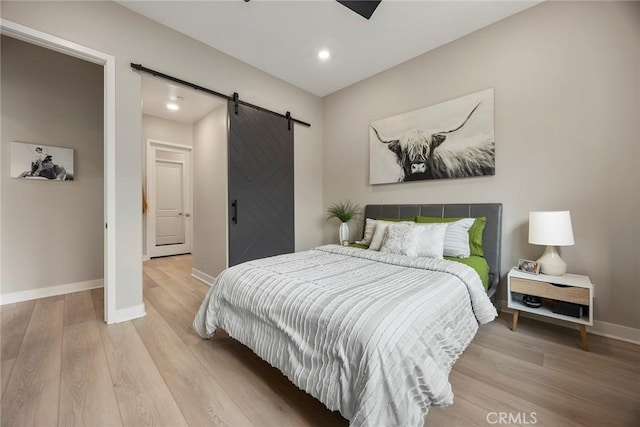 bedroom with baseboards, a barn door, recessed lighting, and light wood-style floors