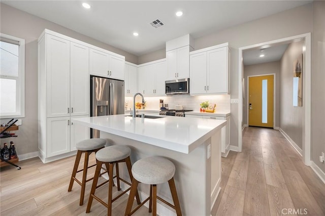 kitchen with a sink, visible vents, white cabinetry, light countertops, and appliances with stainless steel finishes