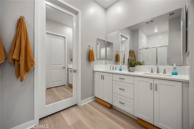 full bathroom with wood finished floors, a sink, visible vents, double vanity, and a stall shower