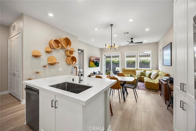 kitchen with a sink, white cabinets, light countertops, stainless steel dishwasher, and hanging light fixtures