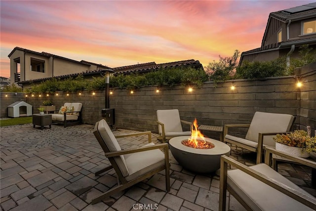 patio terrace at dusk with a fenced backyard and an outdoor living space with a fire pit