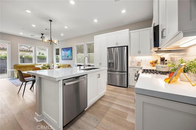 kitchen featuring hanging light fixtures, a kitchen island with sink, stainless steel appliances, light countertops, and a sink