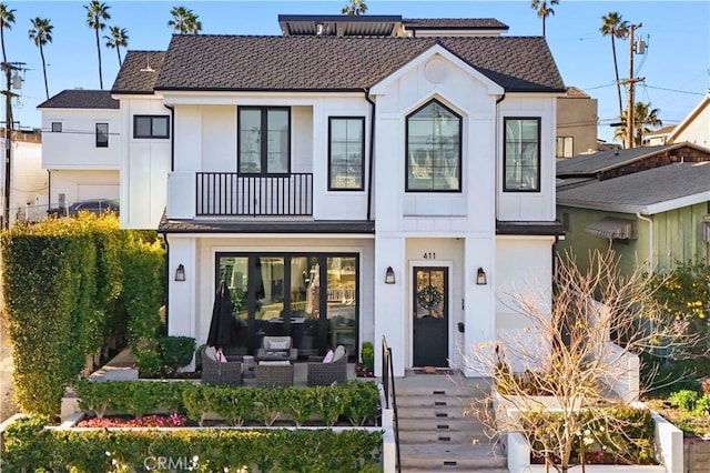 view of front facade with a shingled roof, a balcony, and board and batten siding